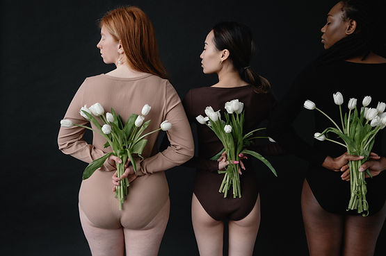 Three women facing away and holding flowers behind their backs. 
