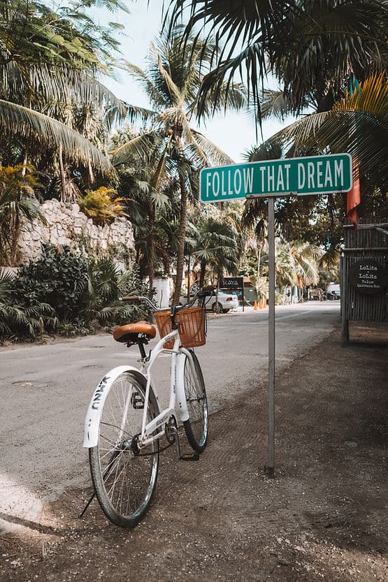 A bicycle sitting under a sign encouraging a person to follow their dream.