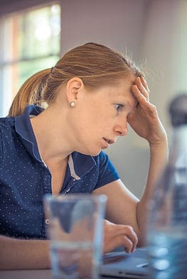 A person with her hand on her head, staring at her computer looking anxious