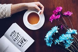 A hand holding a mug and reading a book, learning how to feel more motivated.