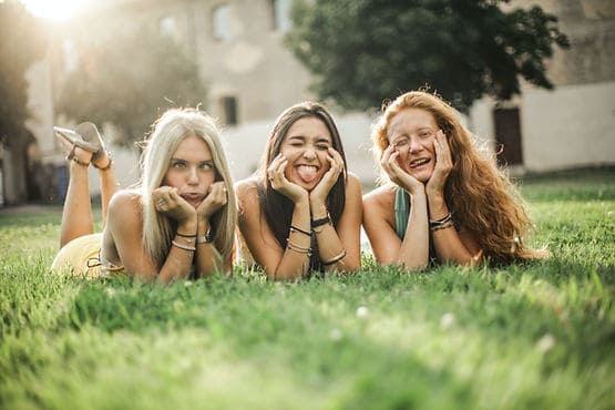 Three young women lying in the grass making funny faces