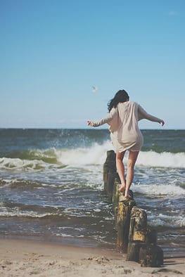 woman balancing on logs over the ocean