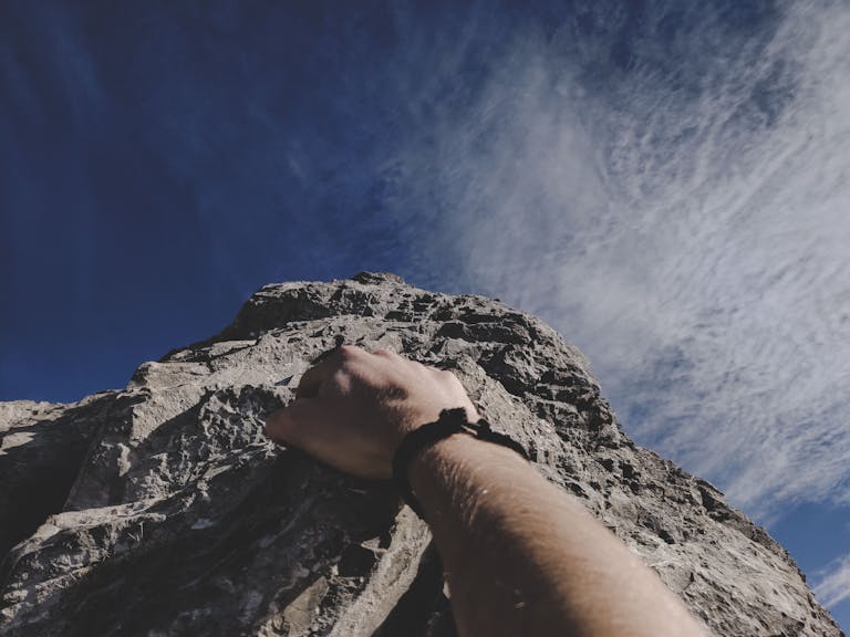 A climber's hand gripping a rocky cliff under a clear blue sky, embodying adventure and building emotional capacity