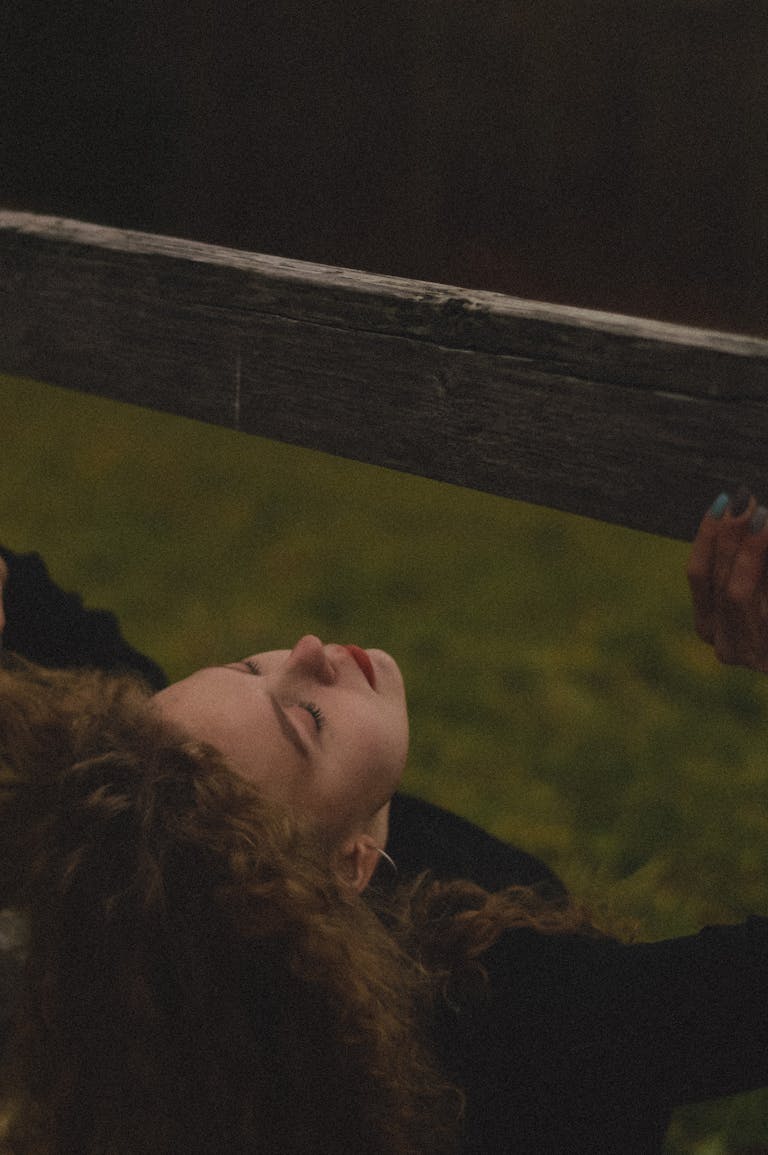 A peaceful outdoor portrait of a woman with curly hair resting with eyes closed, embracing tranquility.