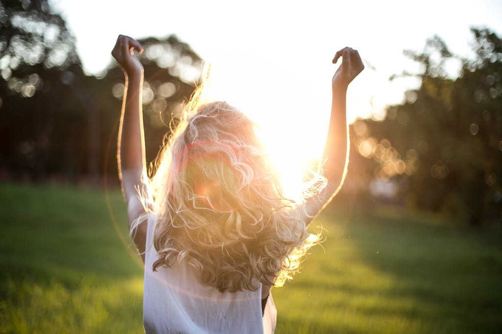 A woman with outstretched arms celebrates the sunset in a grassy field, capturing the essence of the true embodiment definition, freedom, and joy.