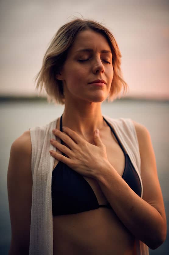 A woman with her hand on her heart, breathing as she navigates the body changes in menopause and embraces the grief and the growth.
