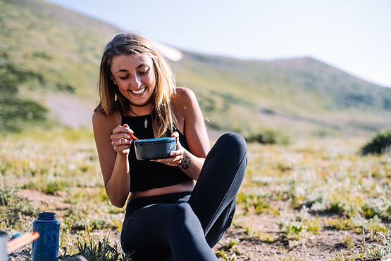 A woman smiling as she eats from a bowl in nature