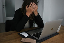 A person behind a laptop with hands over their face in frustration
