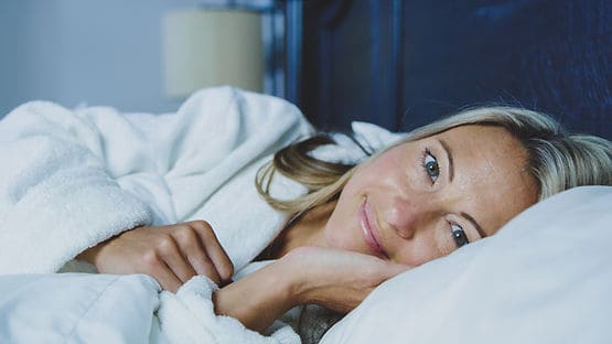 A woman with a gentle restful gaze lying in bed.