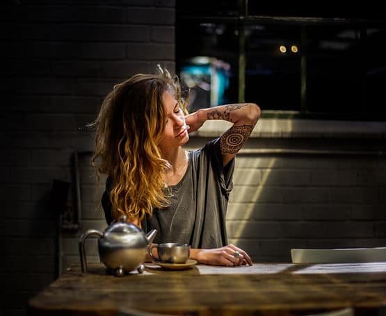 A woman slowing down with tea and touching herself gently to ease the mental load