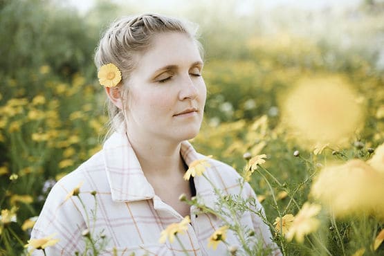 A woman standing in a field of flowers with her eyes closed, feeling her emotions