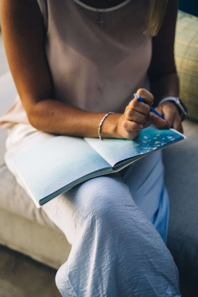 Close-up of a woman sitting with a journal and pen, focusing on reflection and staying with herself as she speaks her truth without guilt.